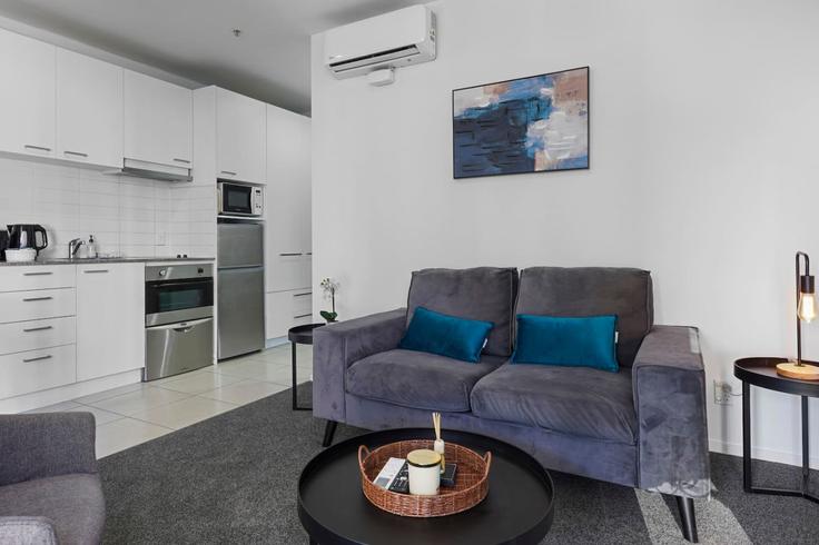 Sala de estar elegantemente projetada com móveis modernos em um apartamento no Building Queen Street - stayhub - 1291932 - NZL em Auckland Central, Auckland Sala de estar elegantemente projetada com móveis modernos em um apartamento no Building Queen Street - stayhub - 1291932 - NZL em Auckland Central, Auckland