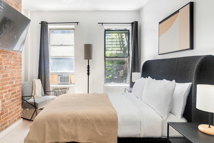 Acogedor dormitorio principal con una cama grande, iluminación suave y muebles con estilo en un apartamento amueblado en 501 1/2 East 83rd en Manhattan, New York